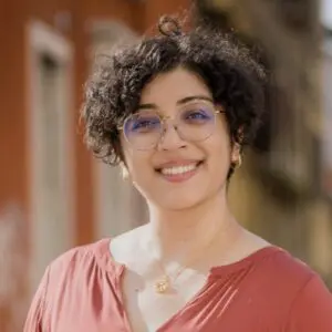 Person with curly hair wearing an orange shirt and glasses