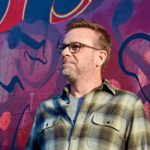 Man in glasses by graffiti wall.