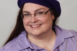A woman wearing glasses and purple shirt with a hat.