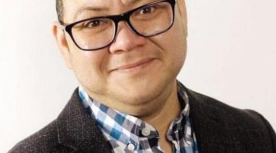 Smiling man in a checkered shirt and blazer.