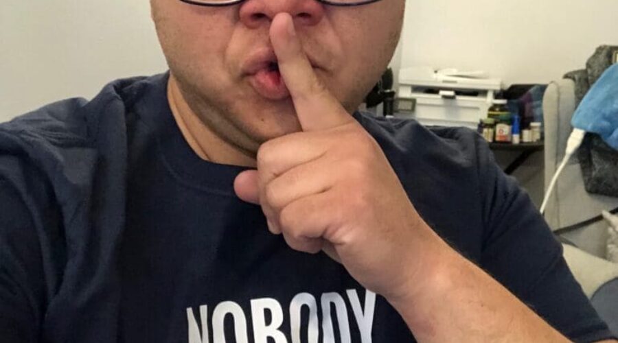 Person making a shushing gesture, wearing a statement shirt.