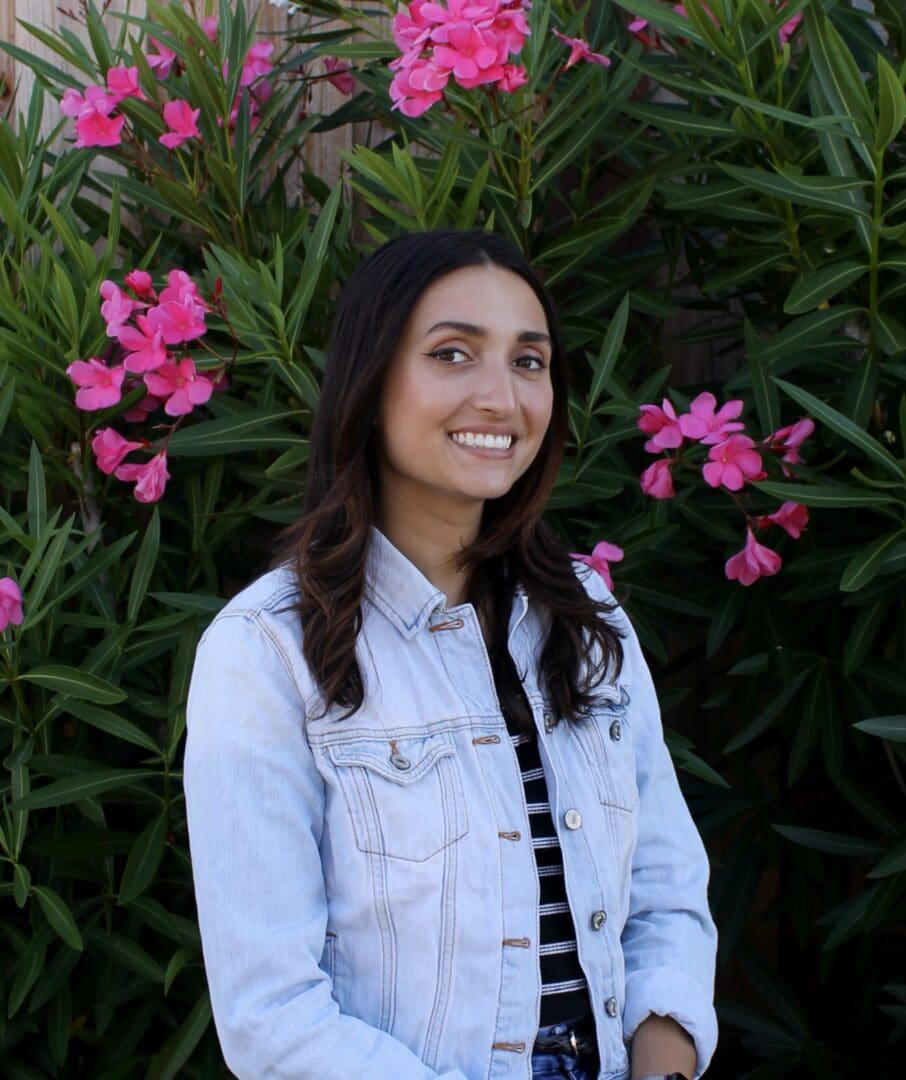 A woman standing in front of some pink flowers.