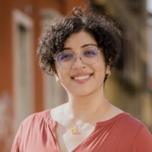 Person with curly hair wearing an orange shirt and glasses