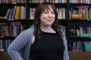 Person with shoulder length hair wearing gray cardigan and dark colored shirt